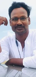 Man in white shirt leaned against a car, posing on a beach with reflection.