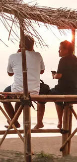 Couple enjoying a beachside sunset under bamboo shelter.