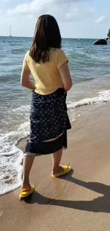 Woman in a yellow shirt walking along a sunny beach shore.