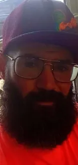 Bearded man in vibrant hat and glasses posing casually.