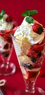 Two berry ice cream sundaes with strawberries and whipped cream in crystal glasses.