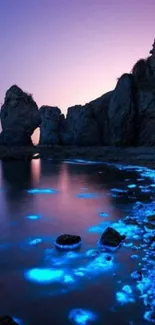 Bioluminescent waves hitting rocky cliffs at dusk with a violet blue sky.