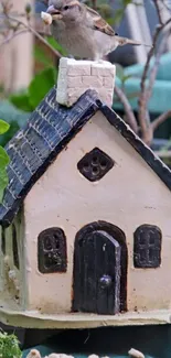 Sparrow perched on a mini rustic house with green backdrop.