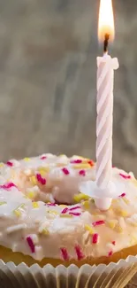 Close-up of a donut with a lit birthday candle and colorful sprinkles.