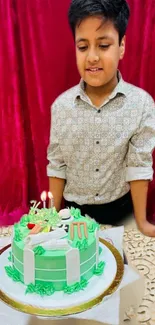 Boy smiling at birthday cake with vibrant red curtain backdrop.