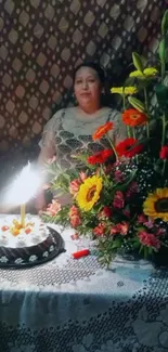 Birthday cake with flowers and lit candle on decorated table.