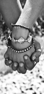 Black and white wallpaper of hands holding with bracelets.