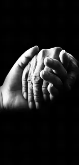A black and white photo of two hands gently holding each other on a dark background.