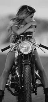 Woman sitting on a vintage motorcycle on an open road in black and white.