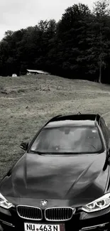 A sleek black car on a scenic forest road, perfect for mobile wallpaper.