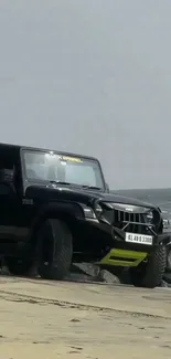 Black jeep parked on a sandy beach with ocean in background.