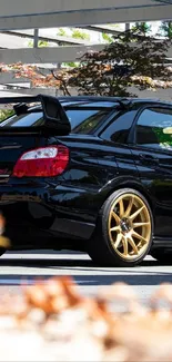 Black sports car with golden wheels under carport.