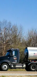 Black truck driving on highway under blue sky with trees.