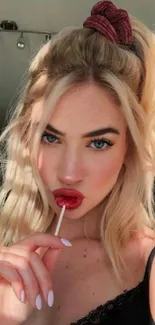 Blonde woman holding a red lollipop in soft lighting.