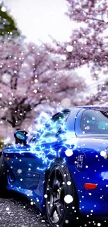 Blue sports car beneath pink cherry blossoms, surrounded by nature.