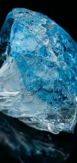 A radiant blue crystal glistens on a dark, reflective surface, creating a serene wallpaper.