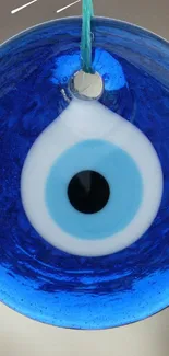 Blue evil eye amulet hanging against blurred background.