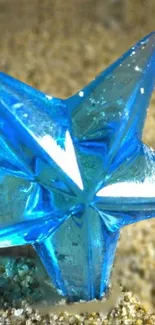 Blue glass star resting on sandy surface wallpaper.