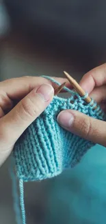 Hands knitting with blue yarn on mobile wallpaper.