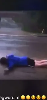 Person in blue jacket lying on wet pavement, enjoying rainy day.