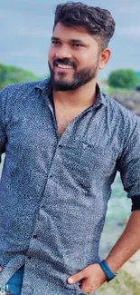 Smiling man in a blue shirt outdoors with a natural background.