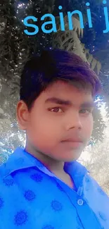 Young man in blue shirt under trees, vibrant wallpaper.