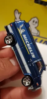 Detailed blue toy van with logo on yellow background.