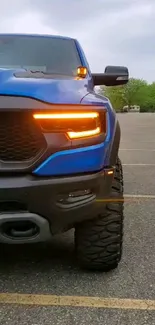 Blue truck front, orange headlights on road, scenic setting.