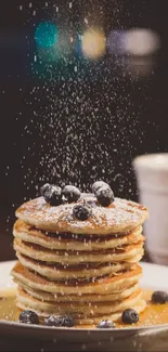 Stack of blueberry pancakes with syrup and powdered sugar.