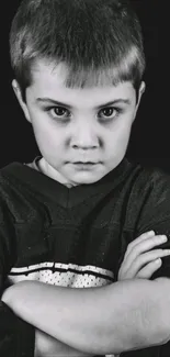 Monochrome portrait of a serious young boy with arms crossed.