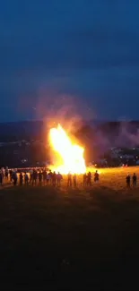 A blazing bonfire against a dark blue night sky with silhouettes of people.