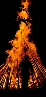 Silhouette standing near a large bonfire at night.