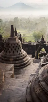 Stone stupas of Borobudur amidst misty morning landscape.