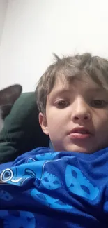 Boy wearing blue shirt with a cat relaxing beside him.