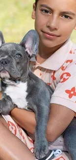 Boy holding a French Bulldog outdoors in sunlight.