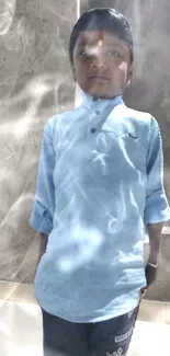 Young boy in light blue shirt standing against a textured wall.