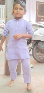 Young boy wearing a light purple outfit standing near a scooter.