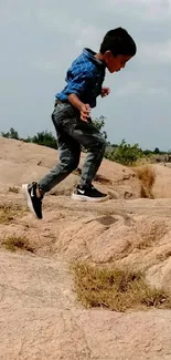 Young boy energetically jumping on rocky outdoor landscape.