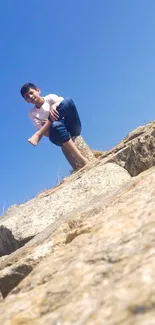 Boy sitting on a rocky cliff under a clear blue sky.