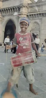 Boy playing drum in front of historic architectural structure.