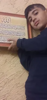 Boy holding framed Islamic calligraphy on textured wall.