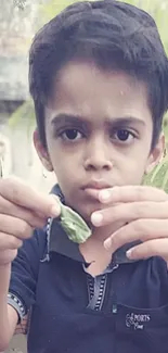 A young boy holds a green leaf in a natural outdoor setting.