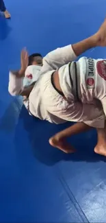 Brazilian Jiu-Jitsu practitioners grappling on blue mat.