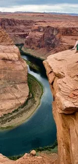 Woman sitting on a cliff overlooking a winding canyon river.