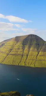 Vibrant green mountain by a blue lake under a clear sky.