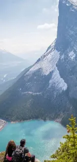 Hikers admire a stunning mountain and lake view in this mobile wallpaper.