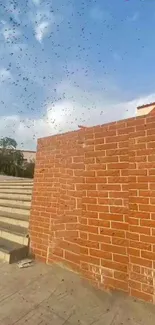 Brick wall with blue sky and scattered birds over steps.