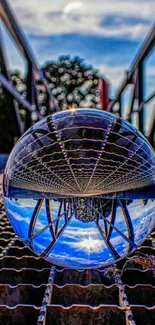 Glass sphere reflecting a bridge and sky on a textured surface.