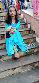 Woman in bright blue dress sitting on steps.