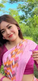 Smiling woman in colorful sari holding a flower outdoors.